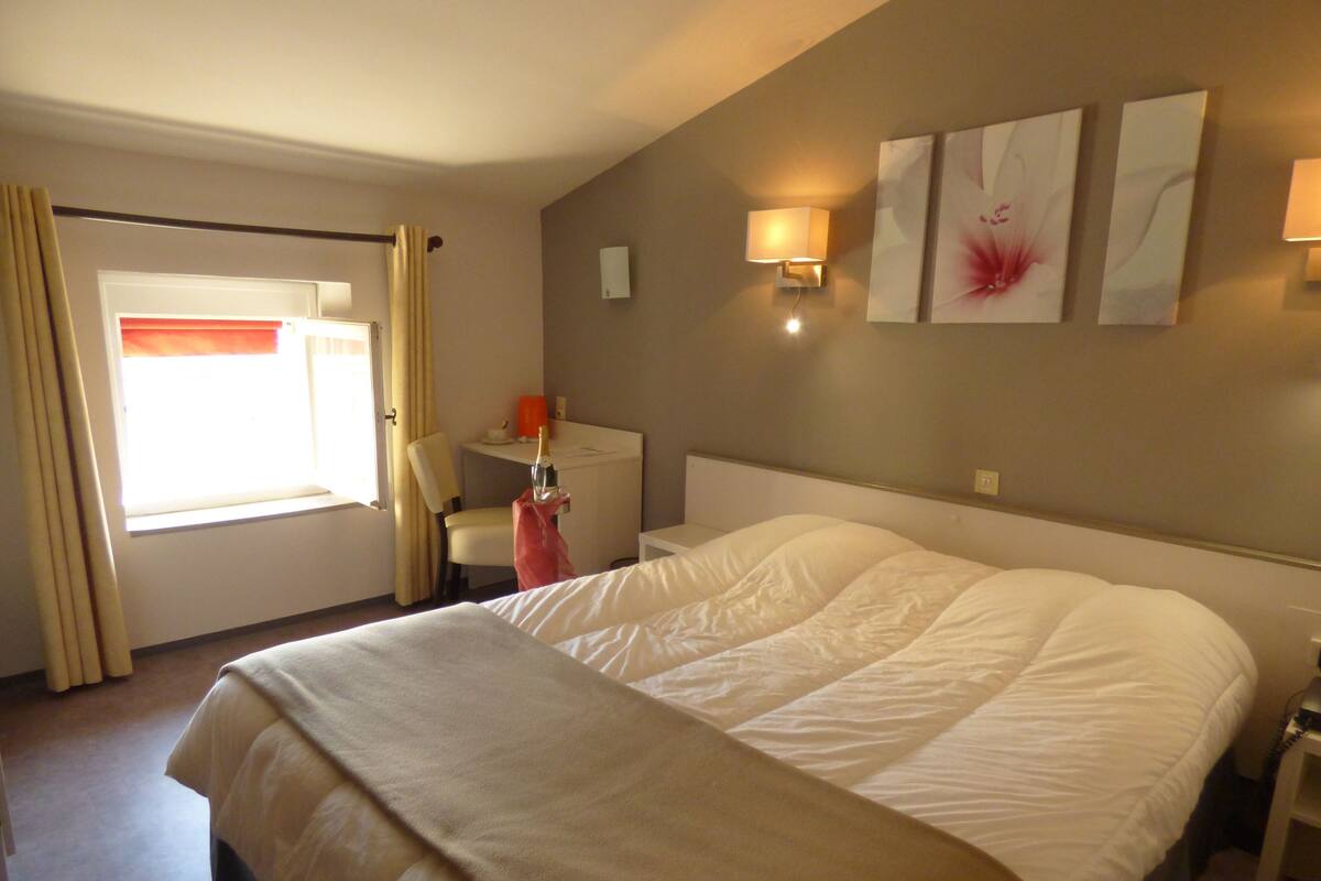 A hotel room with a large bed, a desk, a chair, and a window with curtains.