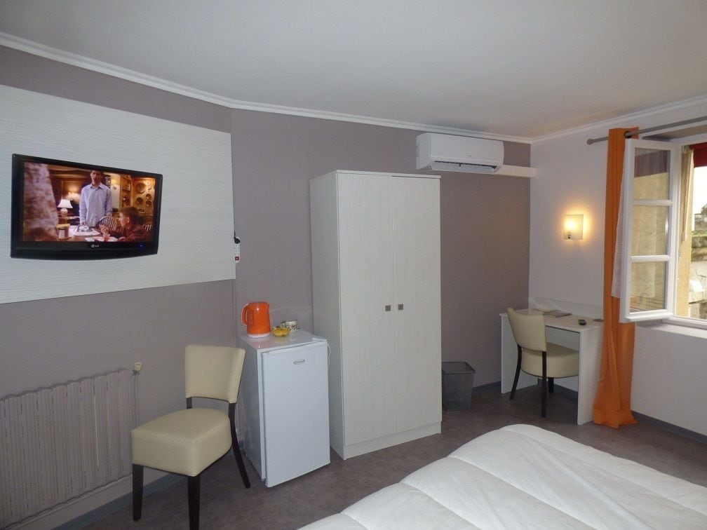 Une chambre d’hôtel équipée d’un lit, d’un bureau, d’une chaise, d’une armoire, d’une télévision et d’un radiateur.