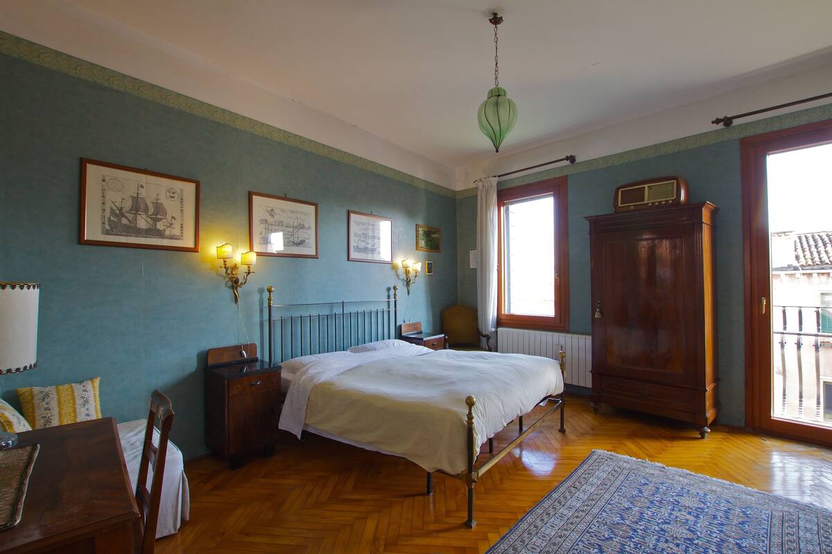 A bedroom with a bed, wooden dresser, and a large window.