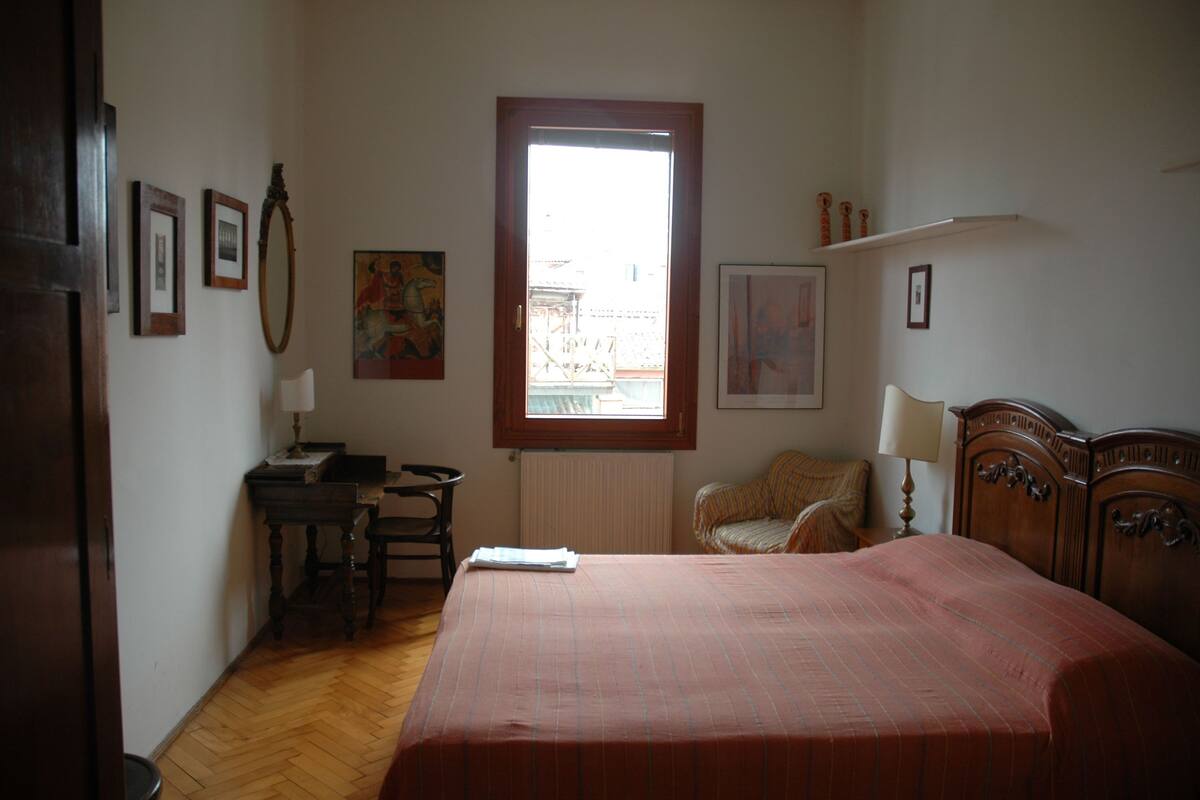 A bedroom with a bed, a desk, a chair, and a window.