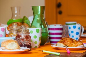 Una mesa con un croissant, una galleta, un tarro de mermelada y una tetera.