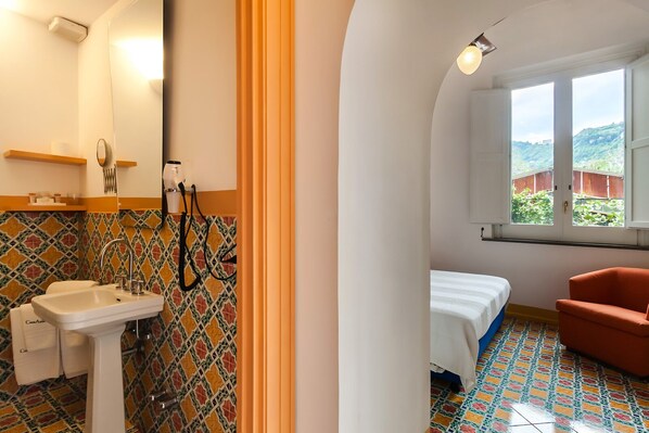 Un baño con lavamanos, espejo y ducha, además de un dormitorio con cama, ventana y sillón.