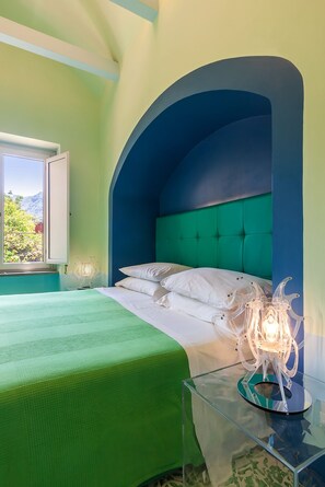 Un dormitorio con una cama, una mesita de vidrio, una lámpara y un ventanal con vistas a la vegetación.