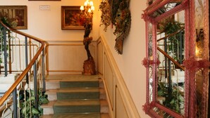 Un escalier dont les marches sont recouvertes d’une moquette verte, avec une rampe en bois et un miroir décoratif orné de motifs floraux.
