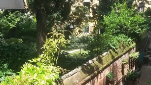 Un mur de briques recouvert de végétation, un chemin et un bâtiment en arrière-plan.