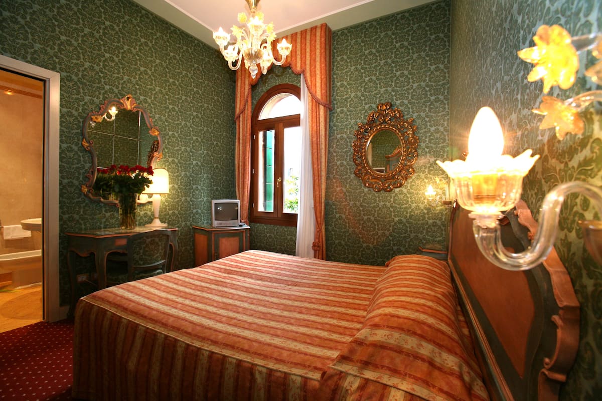 A bedroom with a bed, a dresser, a mirror, a chandelier, and a window with curtains.