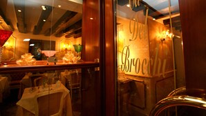 L’intérieur d’un restaurant, avec des tables dressées pour le service, une porte vitrée sur laquelle se reflète le nom « Brocoli », et un éclairage intérieur chaleureux.