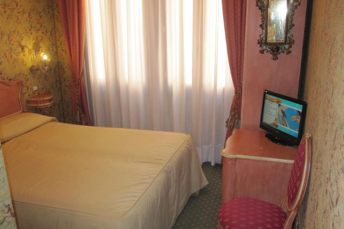 A hotel room with a bed, a desk with a computer, a chair, and a mirror on the wall.