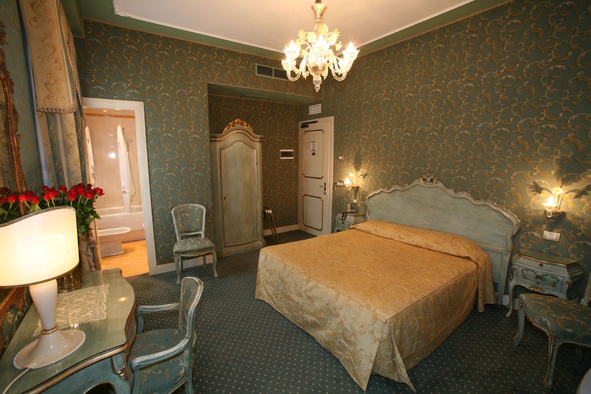 A bedroom with a large bed, a chair, a table with a lamp, a dresser, and a mirror.