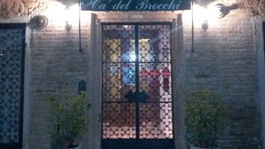 Un bâtiment sur lequel on peut lire l’inscription « Cà del Broccoli » au-dessus d’une porte vitrée, elle-même protégée par un portail en métal. De part et d’autre de l’entrée, on aperçoit deux plantes en pot.