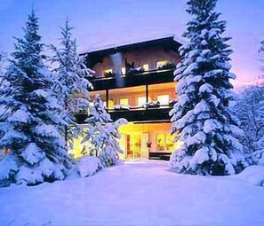 A multi-story building with a snow-covered entrance and surrounding trees. - Biohotel Bavaria (Garmisch-Partenkirchen)