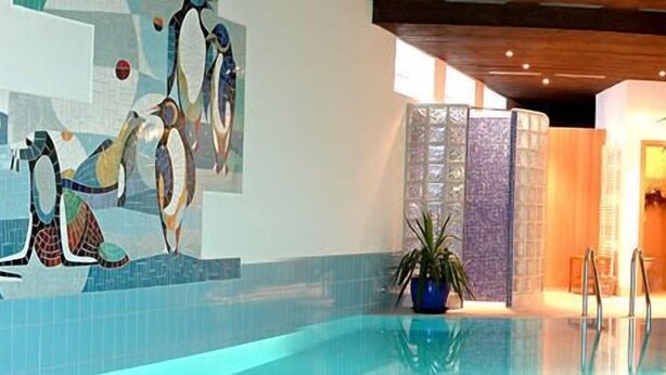 A swimming pool with a tiled floor, a potted plant, and a chandelier. - Hotel Roter Hahn - Bed & Breakfast (Garmisch-Partenkirchen)