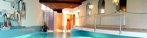 A swimming pool with a tiled floor, a potted plant, and a chandelier.