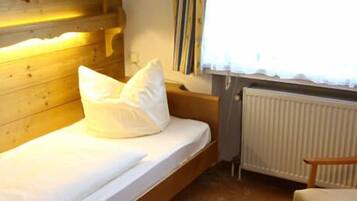 A small, cozy room with a wooden headboard, a single bed with white bedding, a chair, and a radiator.