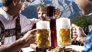 A group of people toasting with beer mugs at a table with a mountain view in the background. - Hotel Roter Hahn - Bed & Breakfast (Garmisch-Partenkirchen)