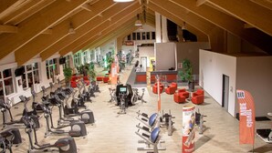An indoor gym with various exercise equipment, wooden beams on the ceiling, and a bright, open space. - Hotel Roter Hahn - Bed & Breakfast (Garmisch-Partenkirchen)