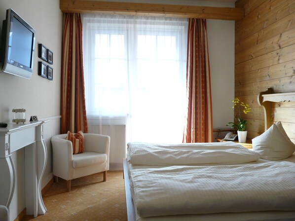 A bedroom with a bed, a desk, a chair, and a television on the wall.