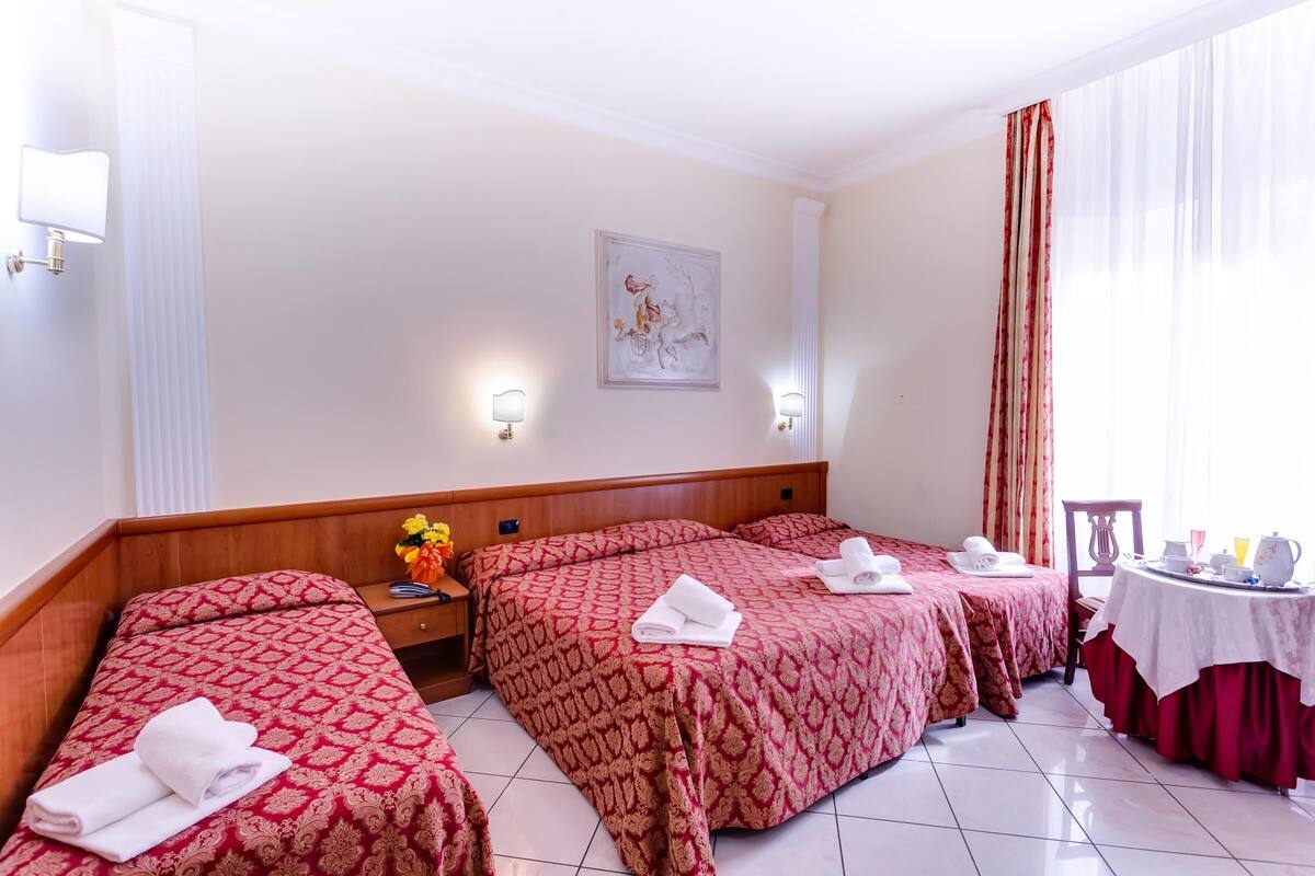 A hotel room with three beds, a dining table, and a painting on the wall.