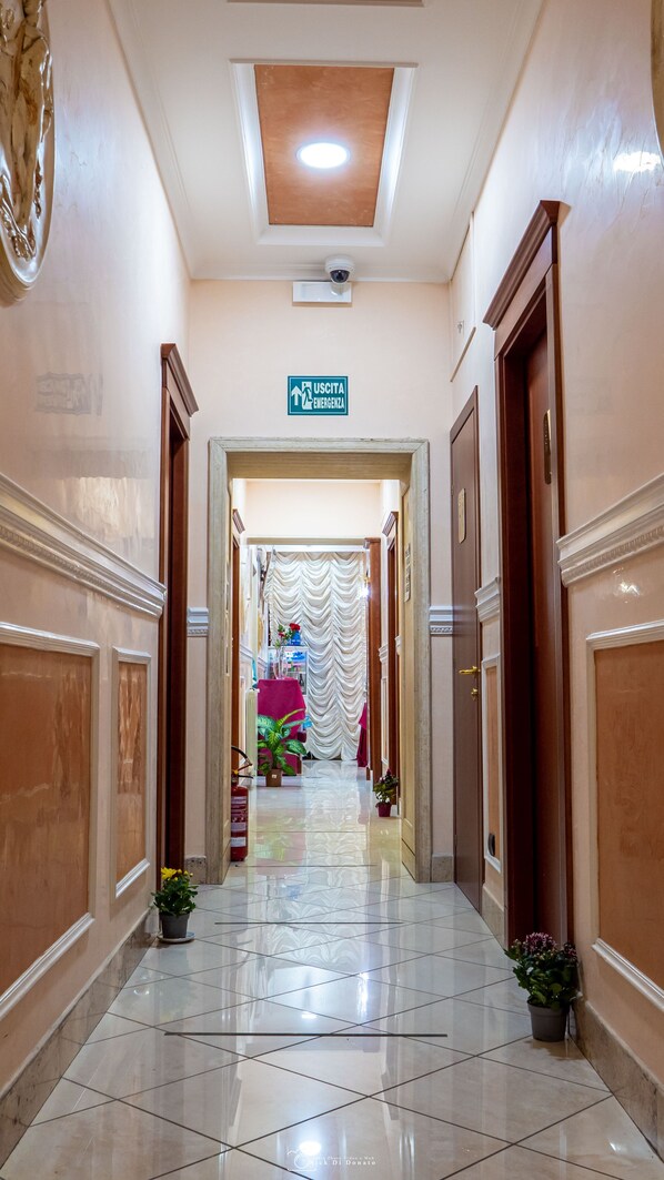 A hallway with a ceiling light, a sign for the emergency exit, and a door on the right. - Hotel Suite Caesar (Rome)