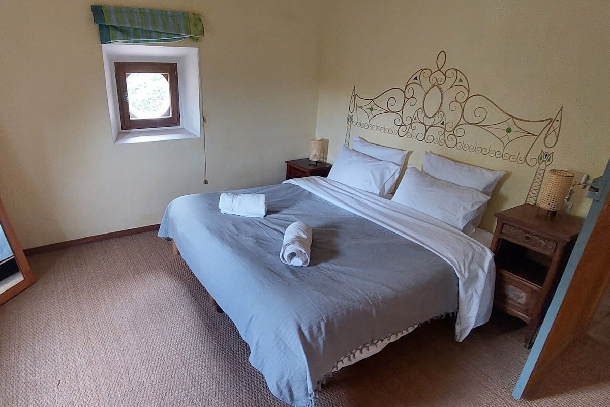 Ein Schlafzimmer mit einem Bett, einem Nachttisch, einem Spiegel und einem kleinen Fenster.