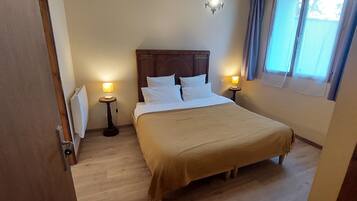 A hotel room with a bed, two bedside lamps, a window with curtains, and a radiator.