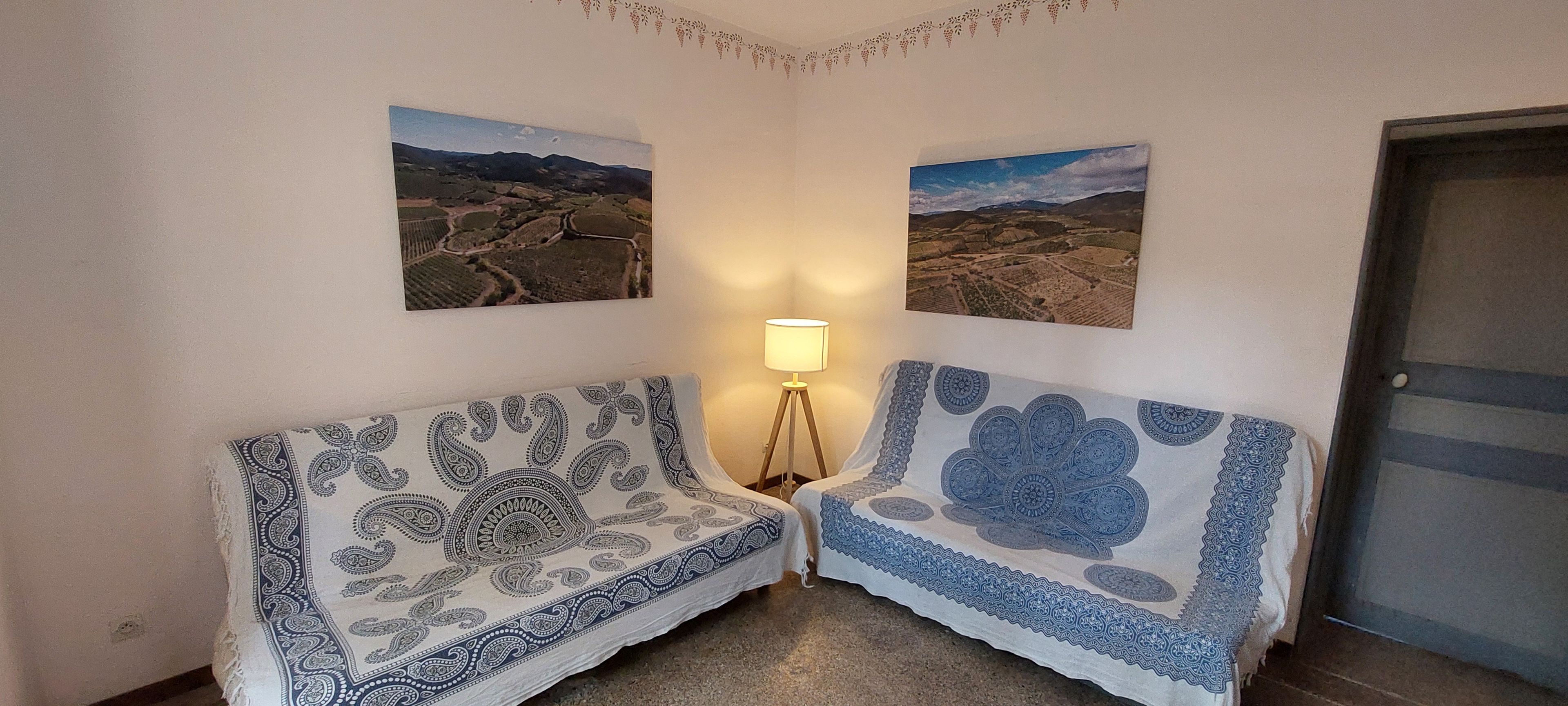 Une pièce d’angle avec deux canapés à motifs, un lampadaire et deux tableaux représentant des paysages accrochés aux murs.