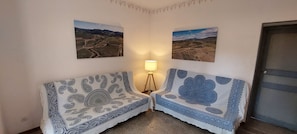Een hoekzaal met twee gestreepten banken, een vloerlamp en twee landschapsschilderijen aan de muur.
