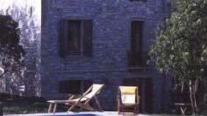 A stone building with a tiled roof, a swimming pool, and lounge chairs.