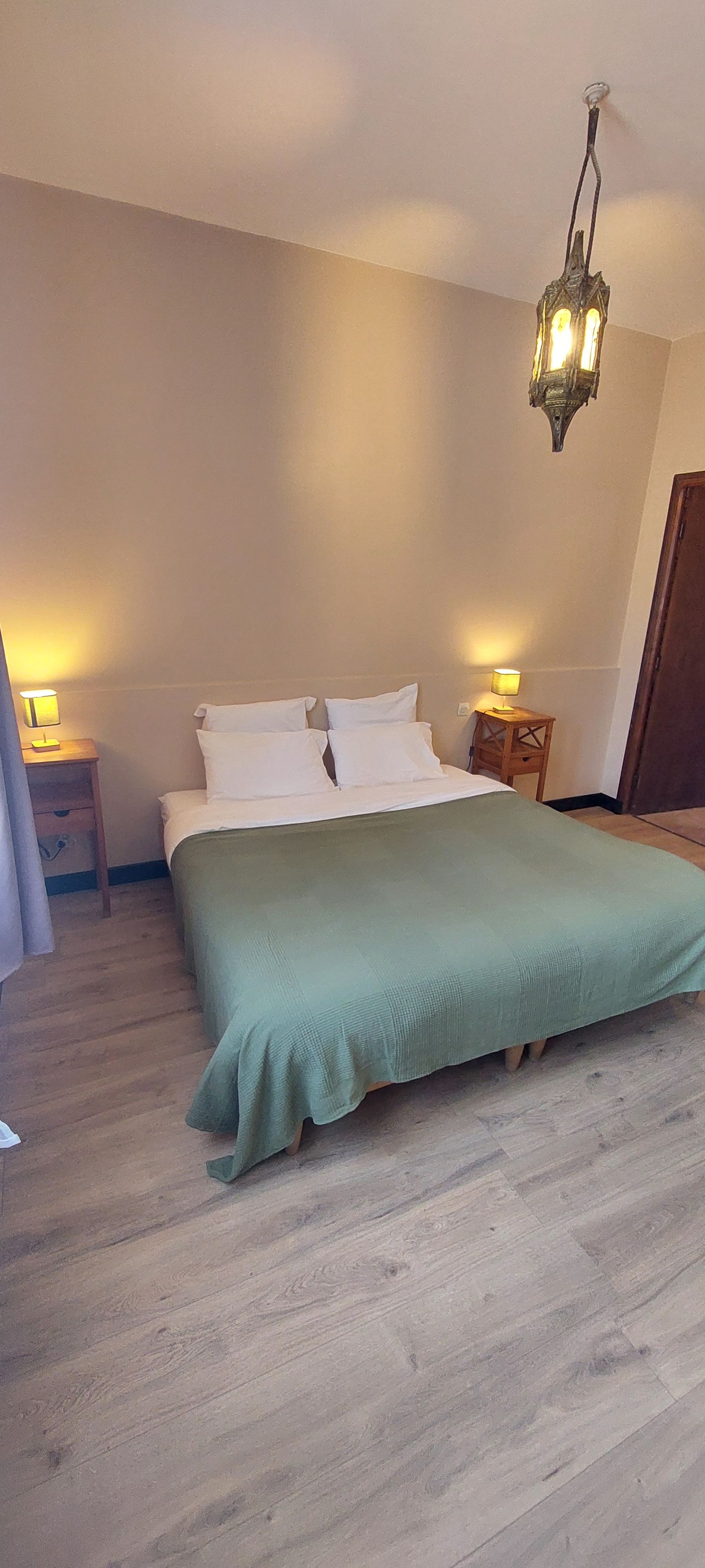 A bedroom with a bed, bedside tables, a hanging light fixture, and a wooden floor.