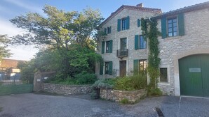 En bygning i sten med grønne skodder, en grøn dør og et skilt, der angiver, at det er et vineri.