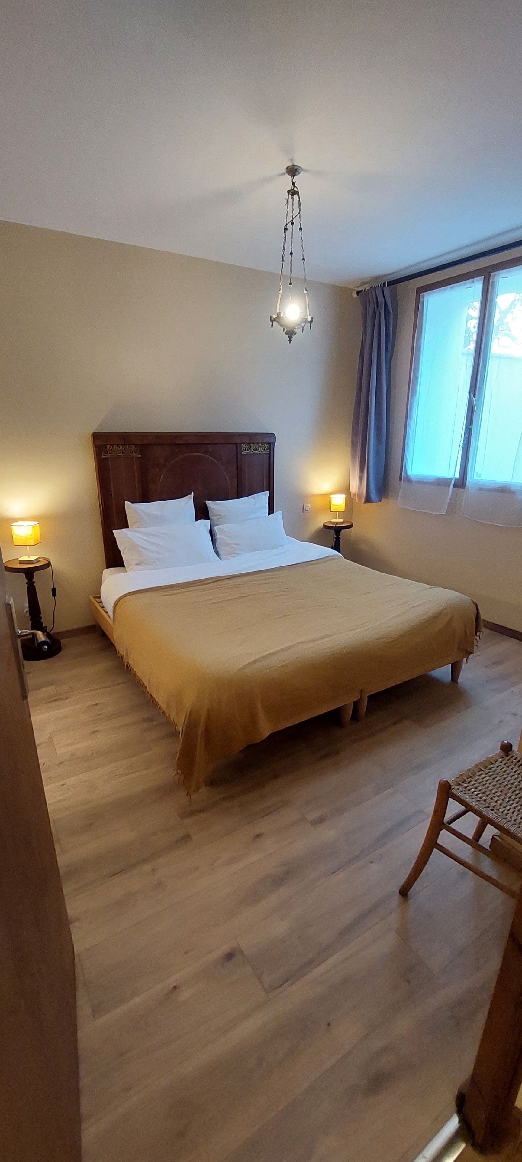 Habitación de hotel con una cama grande, dos lámparas de noche, un cabecero de madera y vistas al exterior a través de una ventana.