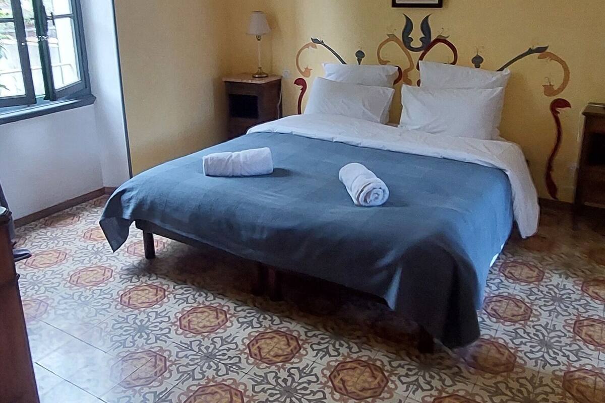 Ein Schlafzimmer mit einem Bett, einem Sessel, einem Nachttisch, einer Lampe und einem Fenster.