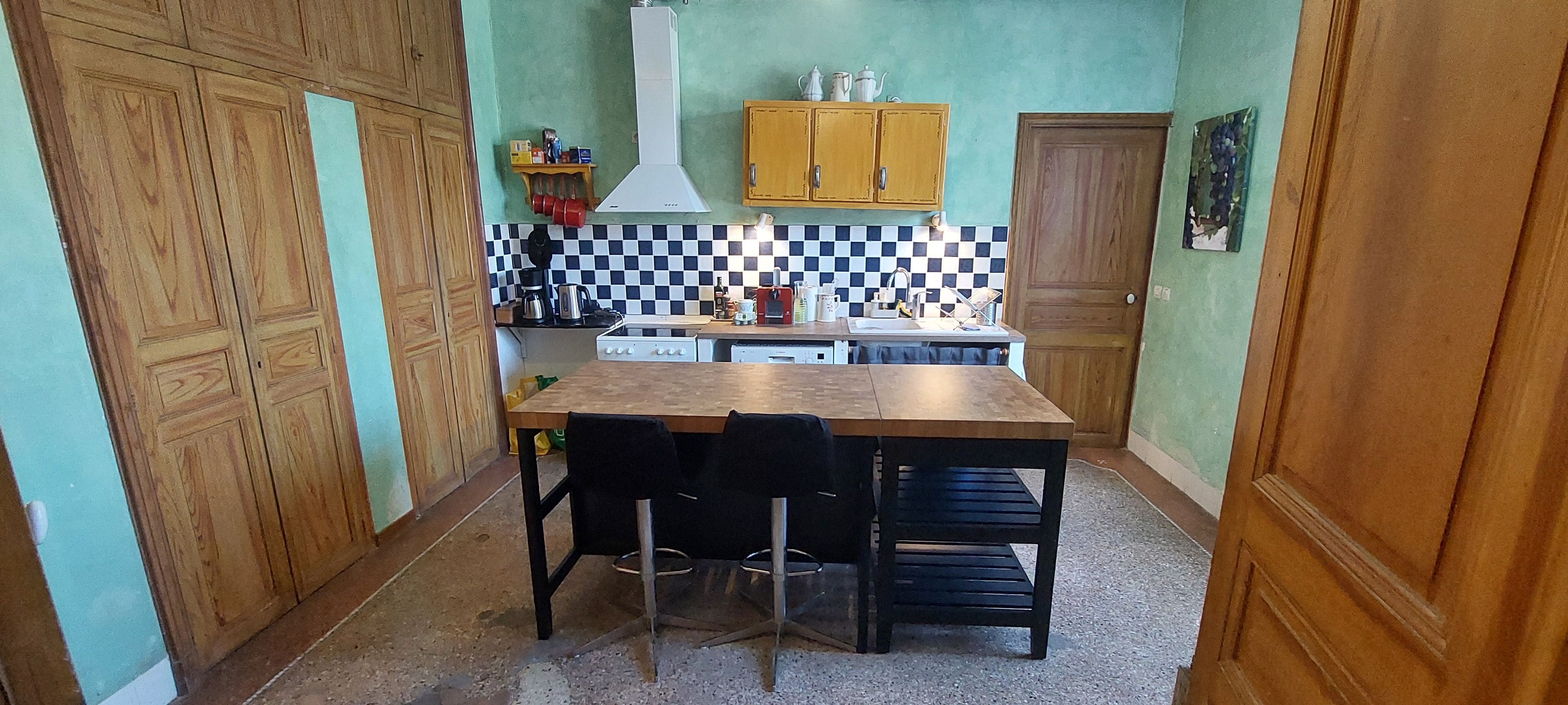 Una cocina compacta con una mesa de madera, sillas, estufa y un salpicadero a cuadros.