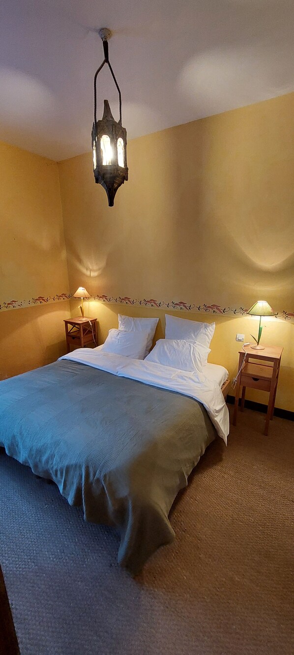 A bedroom with a bed, two bedside tables, a hanging light fixture, and a wall with a floral pattern. - Mas Montluzia (Cascastel-des-Corbieres)
