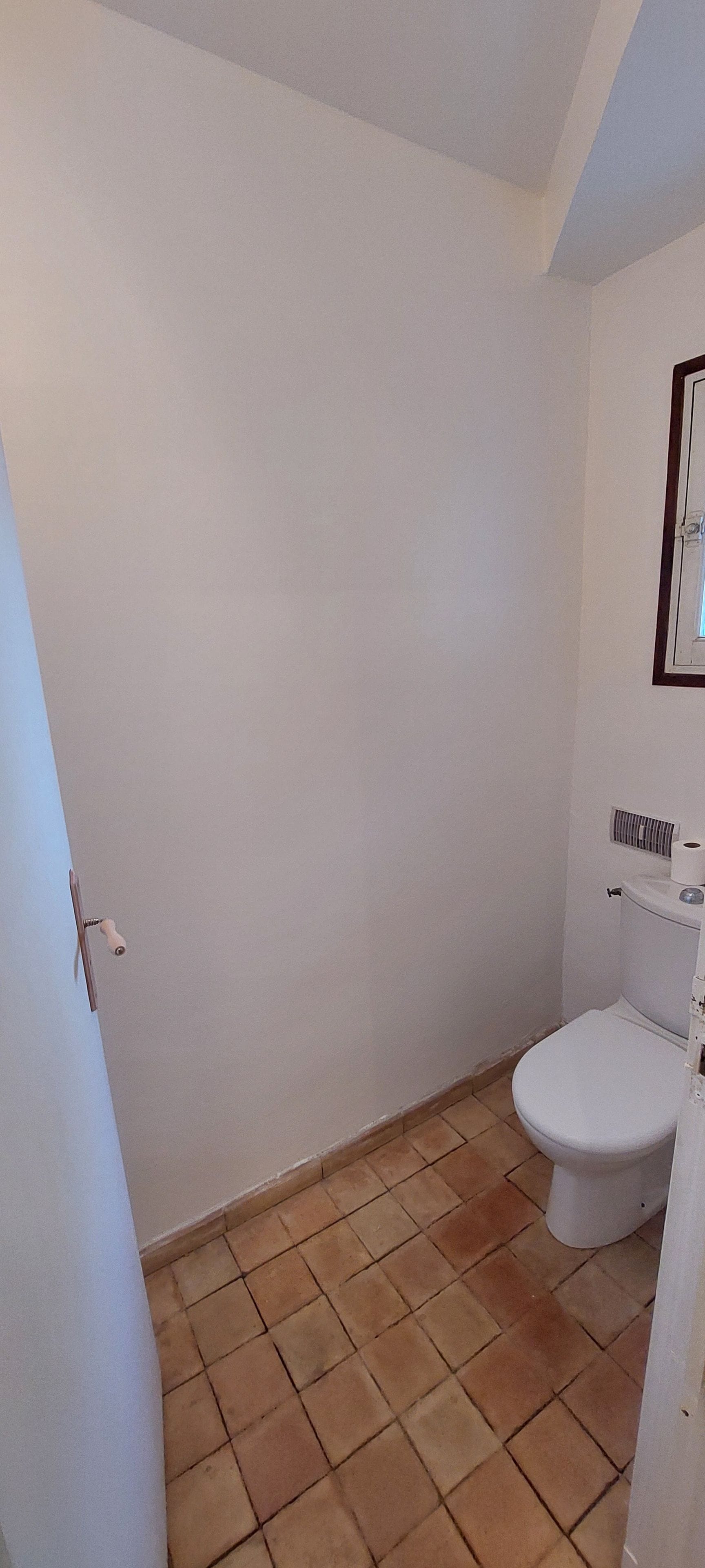 Ein kleines Badezimmer mit weißen Wänden, einer weißen Toilette und einem sichtbaren Lüftungsschacht darüber.