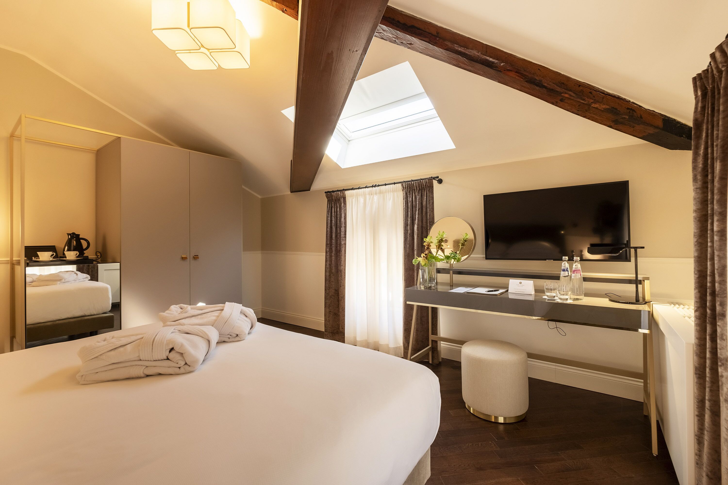 Ein Hotelzimmer mit einem großen Bett, einem Schreibtisch, einem Flachbildfernseher, einem Spiegel und einem Oberlicht.