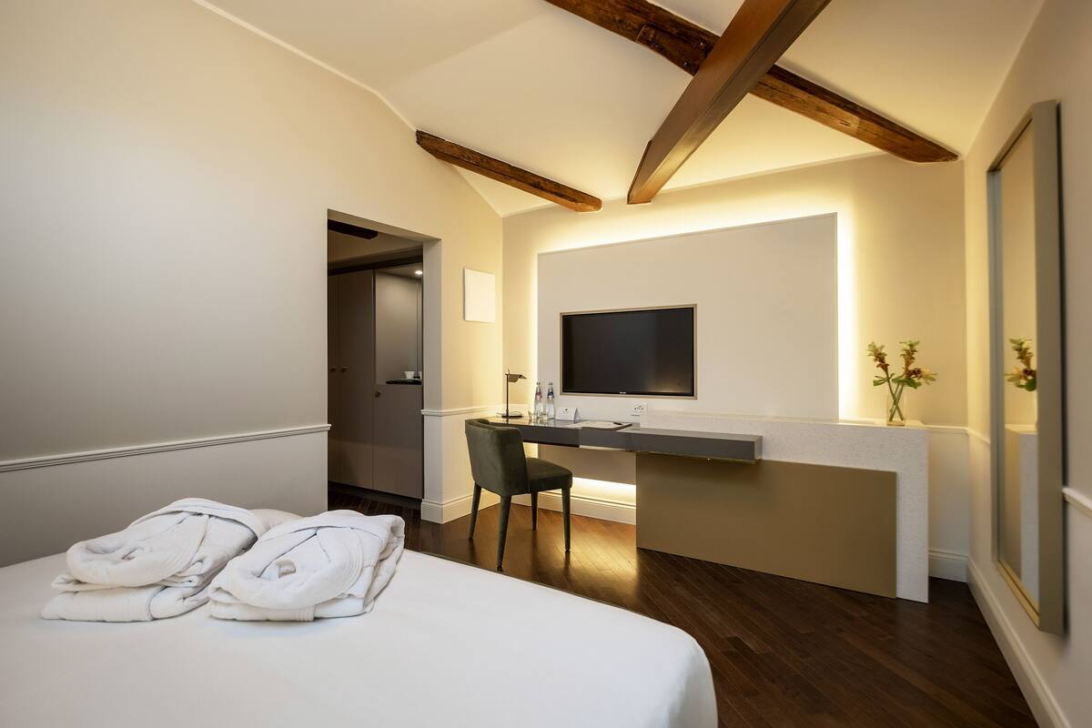 A hotel room with a bed, a desk with a chair, a flat-screen TV, and a small table with a vase of flowers.