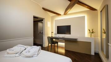 Una habitación de hotel con una cama, un escritorio con una silla, un televisor de pantalla plana y una pequeña mesa con un jarrón de flores.