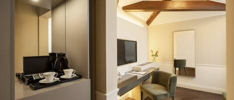 Ein modernes Hotelzimmer mit einem großen Spiegel, einem Schreibtisch mit Flachbildfernseher, einem Stuhl und einer Kaffeestation.