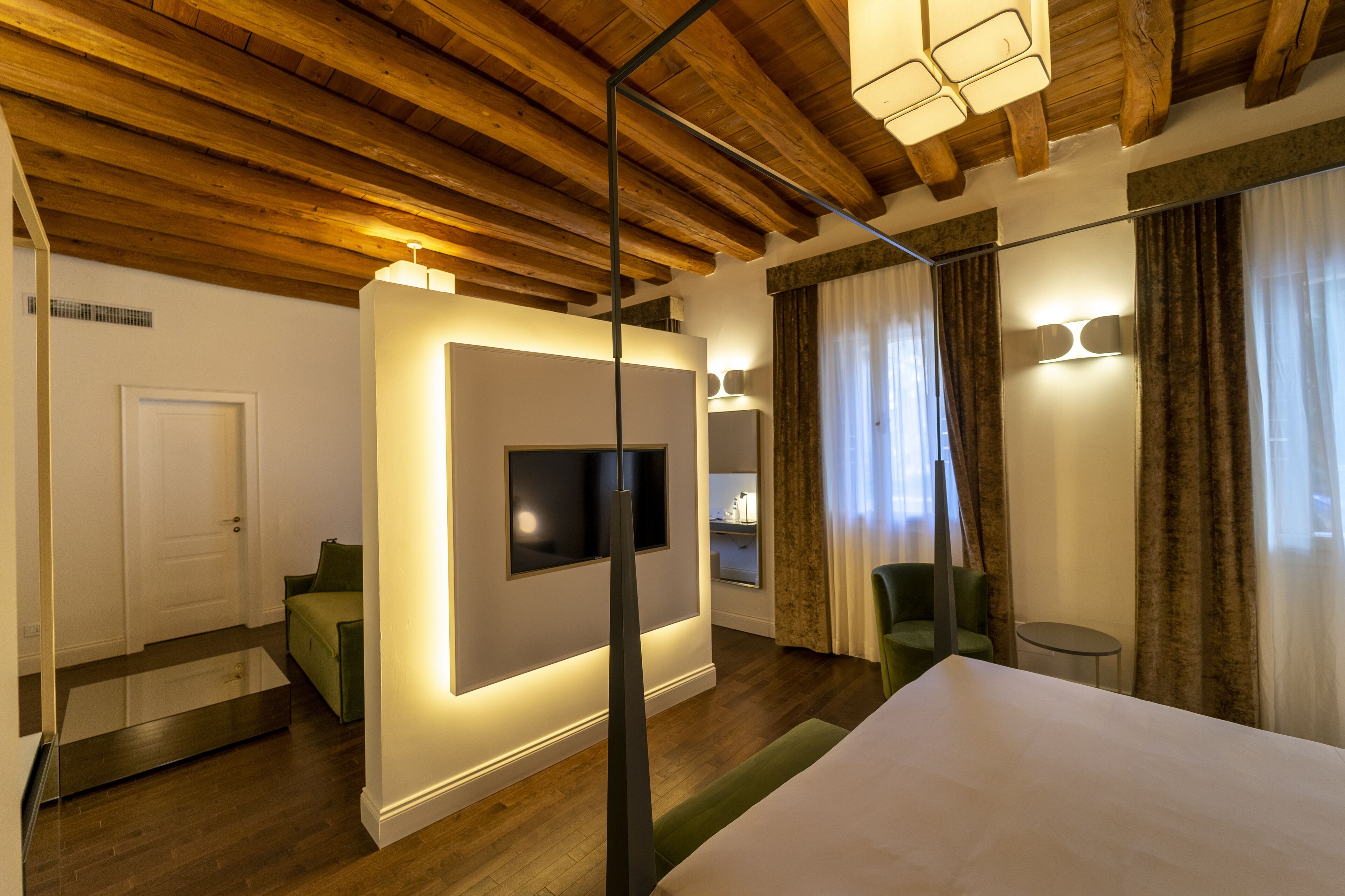 Een moderne hotelkamer met houten balken in het plafond, een groot bed, een flatscreen televisie aan de muur en een klein tafeltje met een stoel.