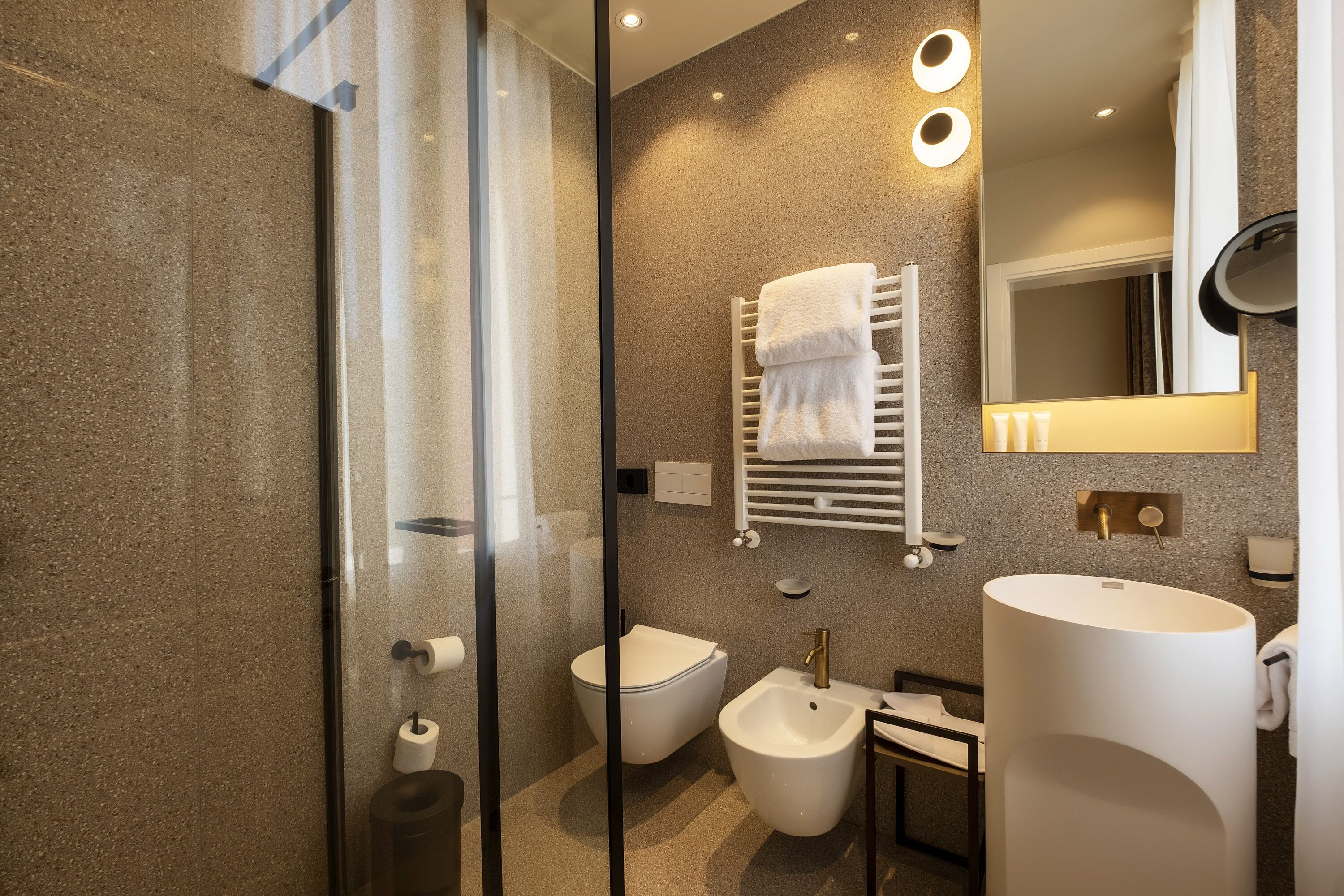 A modern bathroom with a glass shower enclosure, a bidet, a large sink, and a towel rack.