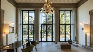 A spacious room with a large window, a chandelier, a dining area with chairs, and a sofa. - Hotel Villa Soligo - Small Luxury Hotels of the World (Farra di Soligo)