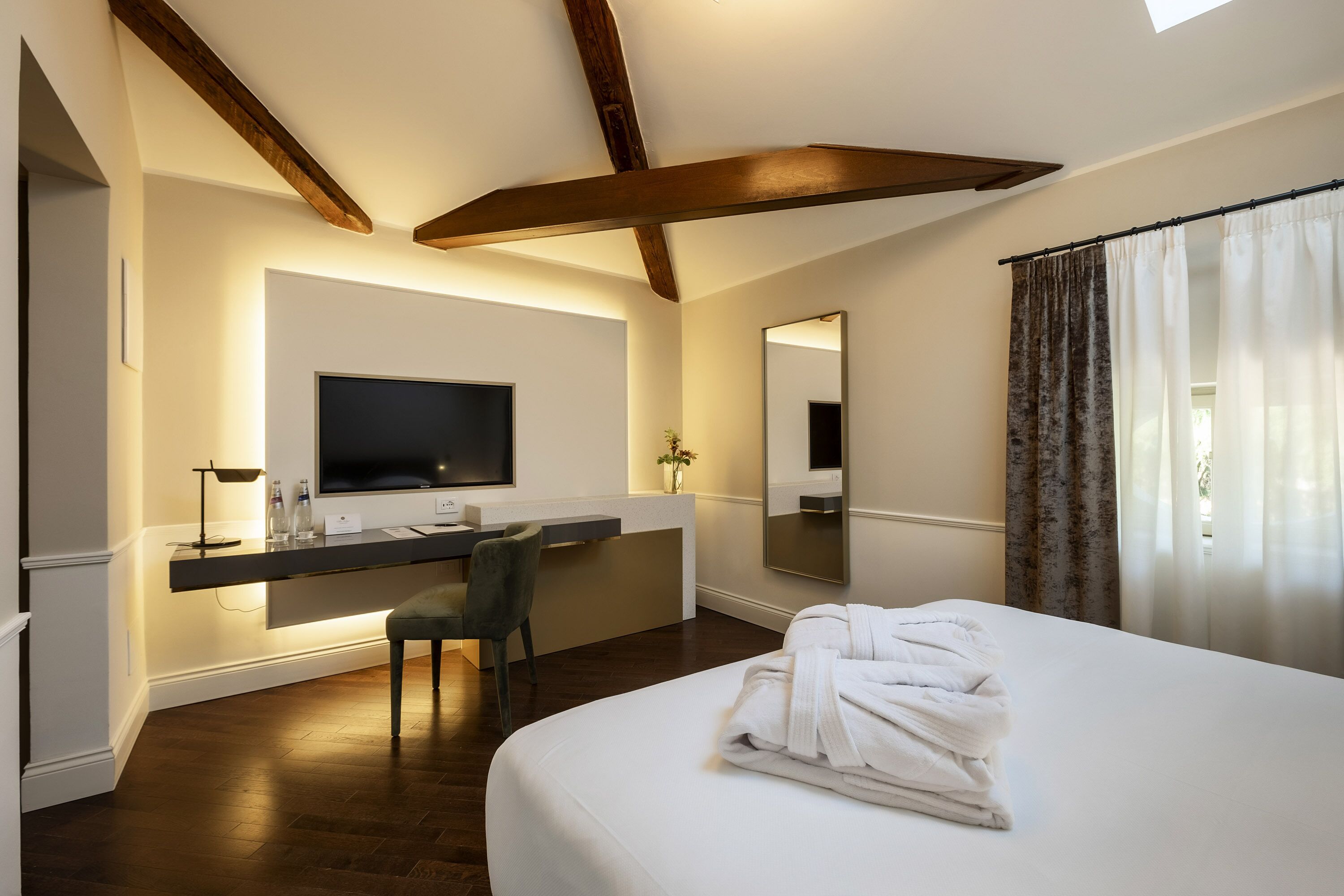 A hotel room with a large bed, a desk with a flat-screen TV, a chair, and a mirror.
