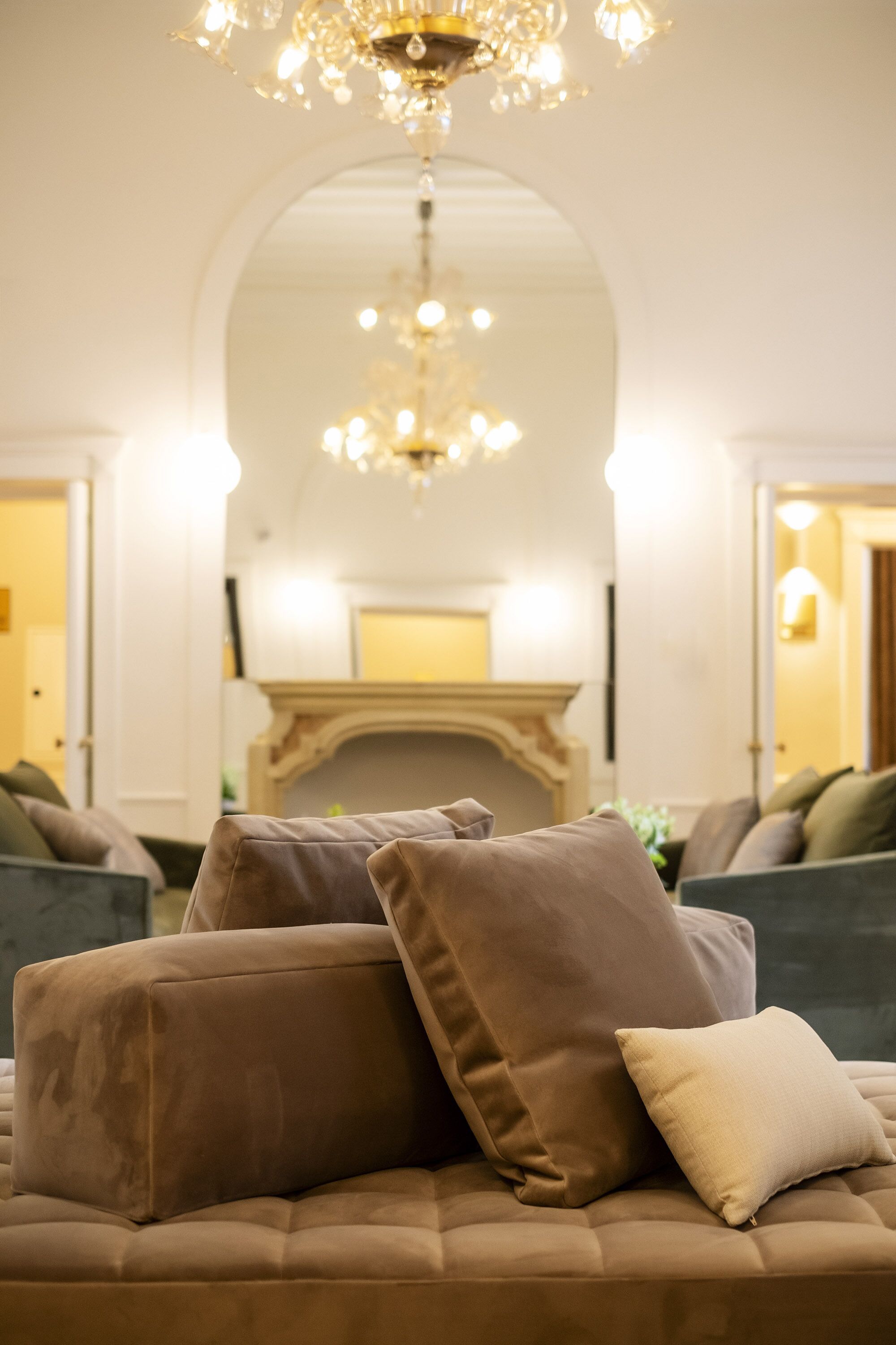 A plush sofa with multiple cushions in a warmly lit room with an arched ceiling and a chandelier.