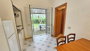 Una cucina compatta con frigorifero, un tavolo con sedie e una porta vetrata scorrevole che dà su un patio esterno con tavolo e sedie.