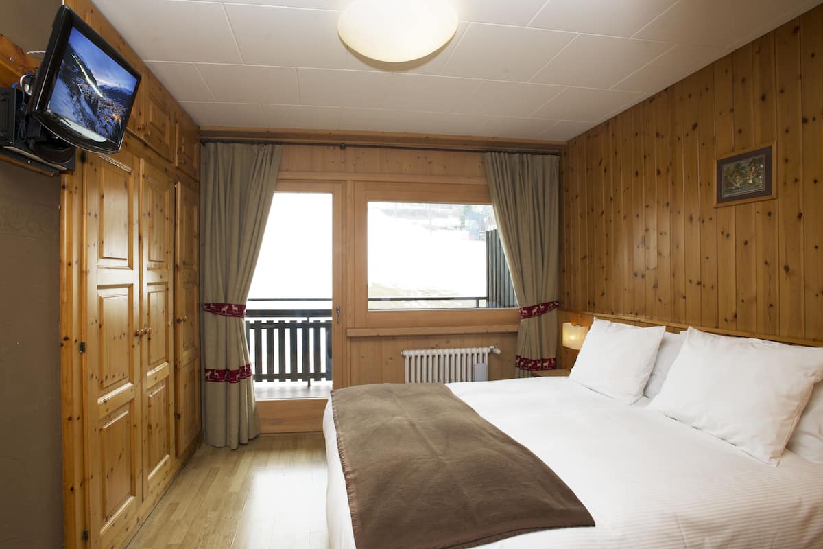 A hotel room with a large bed, wooden paneling, a television, and a window with curtains.