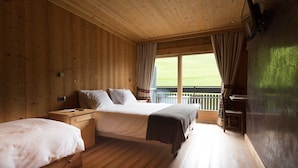 Habitació d'una cabana de fusta amb dos llits, una taula de treball i un balcó amb vista a l'exterior.