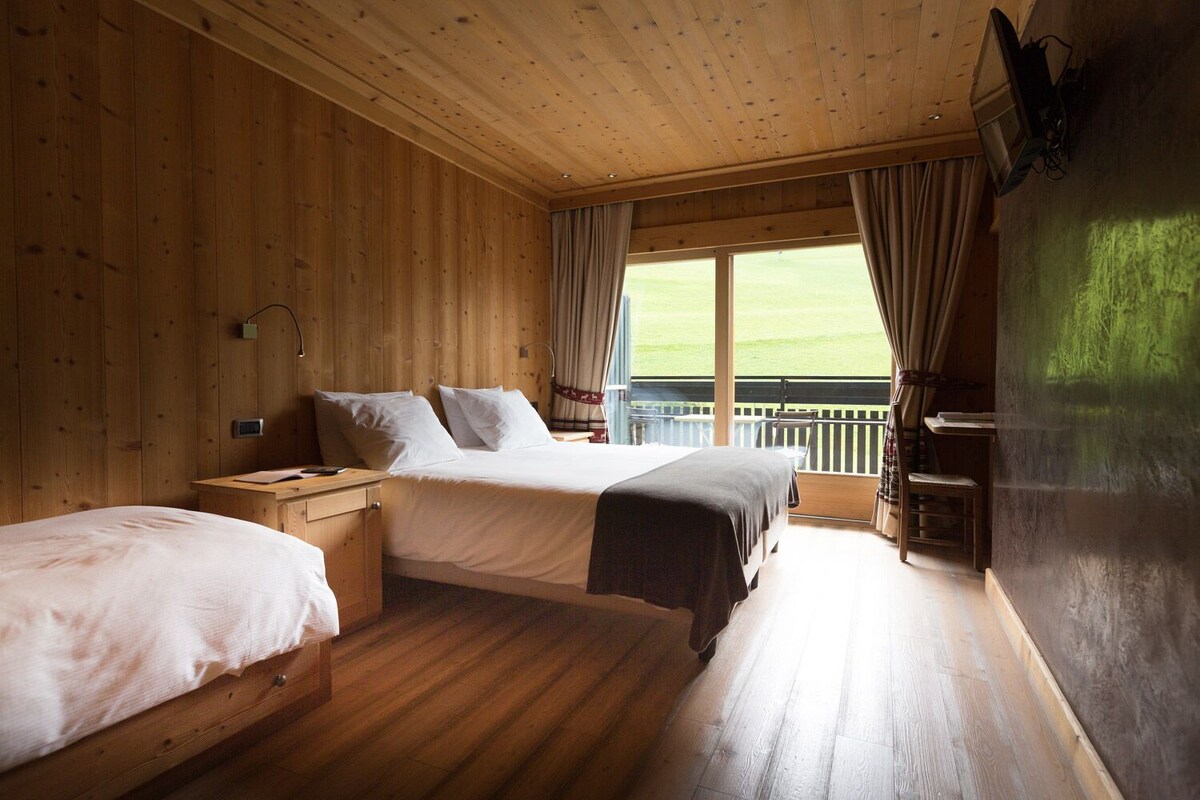 Habitación de cabaña de madera con dos camas, un escritorio y un balcón con vistas al exterior.