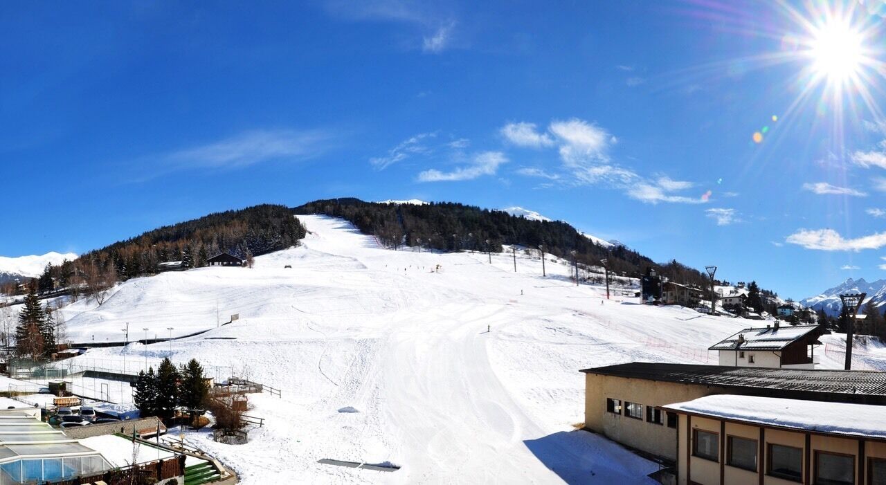 Pista de esqui coberta de neve, céu claro e sol brilhando.