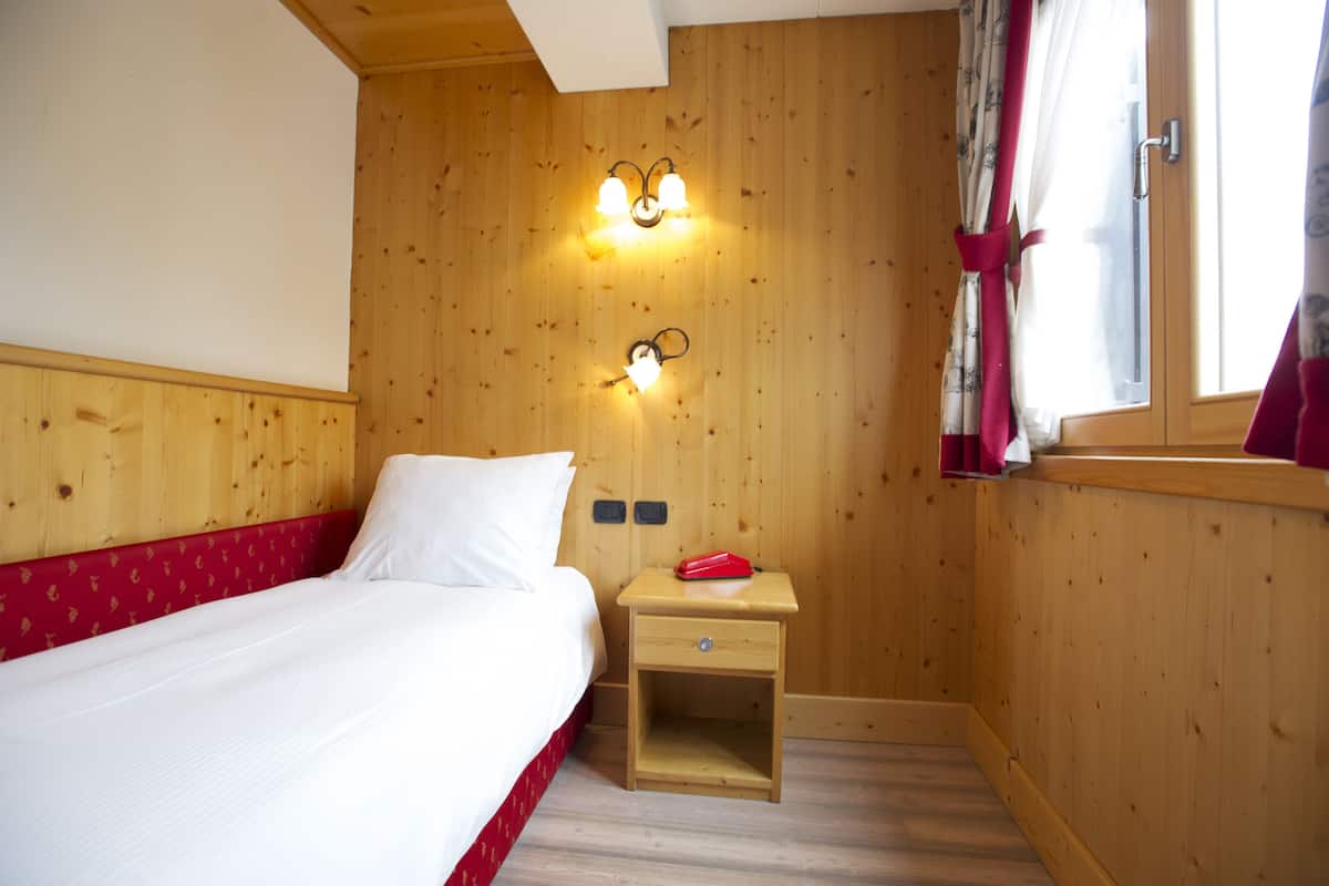A wooden-paneled room with a bed, a nightstand, and two wall-mounted light fixtures.